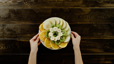 hands holding plate of fruits on the brown wood table top viewの写真素材