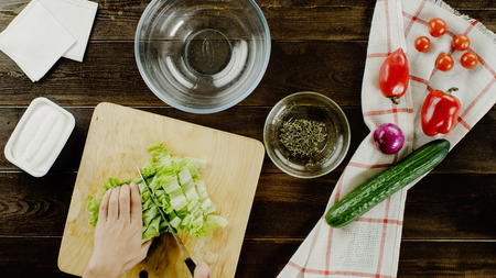 table with vegetables and hands preparing Greek salad top viewの写真素材