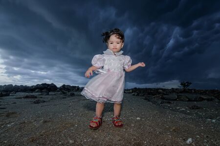 A baby girl are standing by the stormy sea and looks into the cameraの写真素材