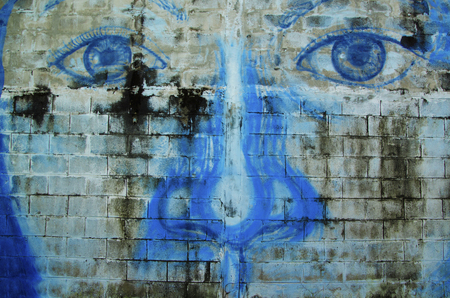 Street Art painting the eyes and nose of a woman painted in blue on a brick wall.のeditorial素材