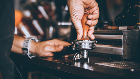 Professional Barista pressing tamping freshly ground coffee beans in a portafilter in coffee shop or cafe.の写真素材