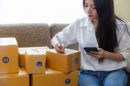 Asian young woman startup small business online at home and packing box for delivery online to...