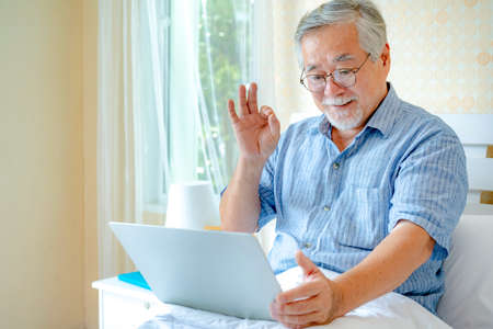 Happy old man positive, Portrait Asian Senior man and eyeglasses using computer laptop in bedroom at...