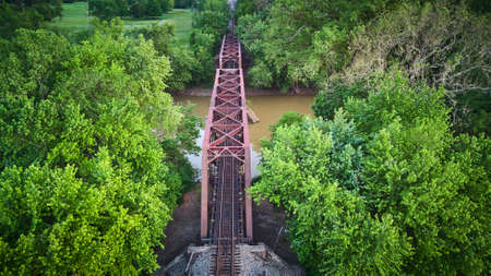 Aerial of purple metal bridge for train tracks over brown river with green treesの写真素材