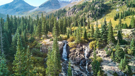 Waterfall tucked into valley of mountains surrounded by pine treesの写真素材