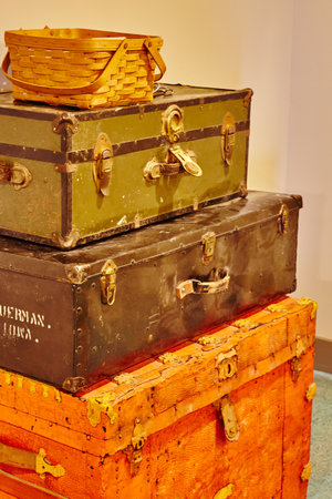 Stack of three antique trunks, red, black, and green, with a basket on top in yellowed lightingの写真素材