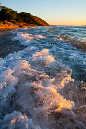 Foamy white crest of waves crash against the beach with a mountain in the backgroundの写真素材
