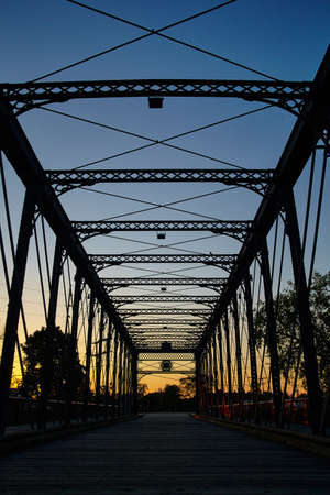 Metal bridge extends into the distance, silhouetted by the orange setting sunの写真素材