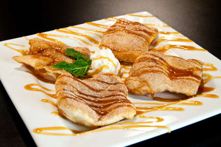 Fried dough dessert dusted with cinnamon sugar and drizzled with chocolate and caramel sauces on a white plateの写真素材