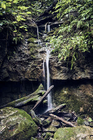 Mystical small waterfall over rocks into logs and bouldersの写真素材