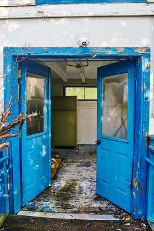 Old abandoned blue double doors leading into a dilapidated room with white floors and wallsの写真素材