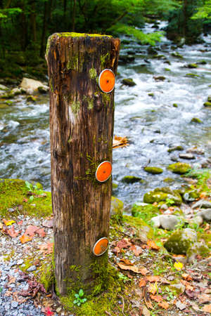 Vertical sign post with fluorescent orange markers stands in front of a rushing riverの写真素材