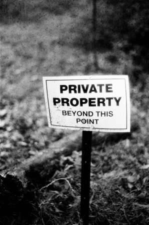 Black and white shot of a Private Property sign staked into a leaf covered groundの写真素材