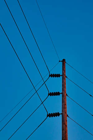 Power lines attach and divert on a telephone pole on a clear blue sky dayの写真素材
