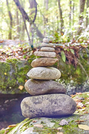 Serene stack of oval shaped rocks with trees and a river in the backgroundの写真素材