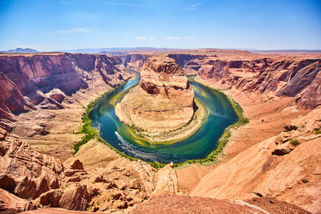 Orange canyons surrounding Horseshoe Bend river with rocky outcropping in the middleの写真素材