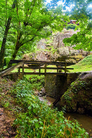 Bridge over creek with stone wall and structure on cliff in green forestの写真素材