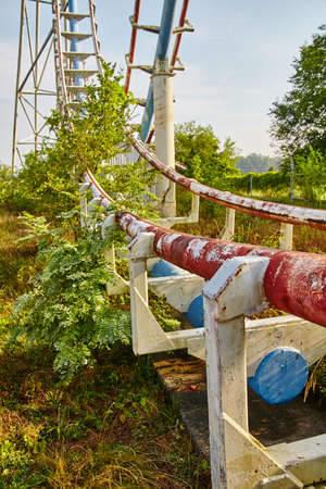 Rusted rails of an abandoned roller coaster with green leaves and shrubsの写真素材
