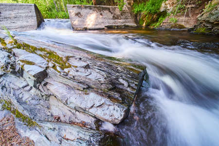 Cement dam funneling river with large outcropping of stone covered in mossの写真素材