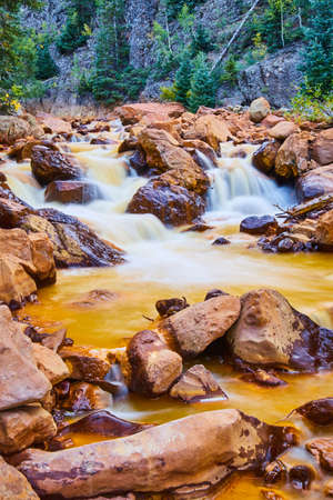 Red stones along golden river with cascading waterfallsの写真素材