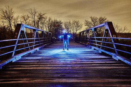 Glowing blue light surrounds a man in the middle of a metal bridge at duskの写真素材