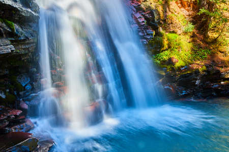 Detail of waterfall against cliff rocks with red sheets of rock and bright blue water