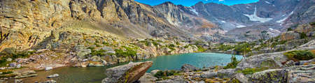 Panorama of lake in the mountains with boulders and snowの写真素材