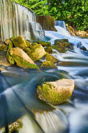 Algae rocks next to manmade waterfalls and smooth waterの写真素材