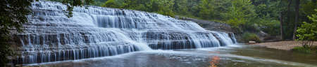 Panorama of large cascading waterfall over rocks in green forestの写真素材