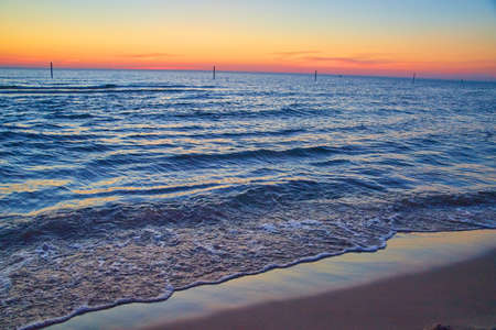 Lake beach with waves of water and sunset or sunrise colors on horizonの写真素材