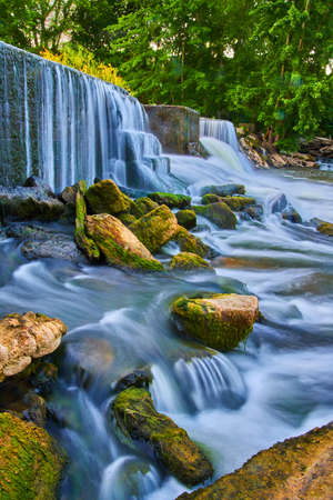 Algae rocks sticking out of waterfalls from manmade damの写真素材