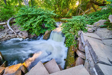 Waterfall surrounded by rubble and cement tiles in green forestの写真素材
