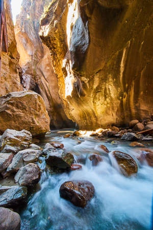 Close view of waterfalls over red rocks at bottom of deep canyon with golden sunlightの写真素材