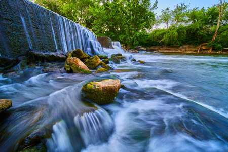 Texture of rocks covered in moss sticking out of waterfalls by manmade damの写真素材