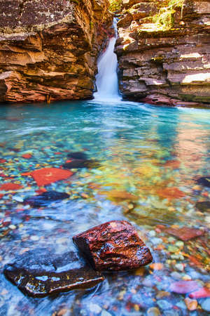 Colorful river rock in focus with large waterfall and cliffs at bottom of gorgeの写真素材