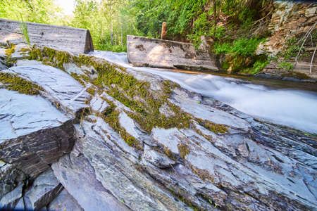 Stone jutting out of river with detail of moss and cement dam in backgroundの写真素材