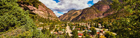 Panorama of small mountain town tucked in mountains with lush green forestsの写真素材