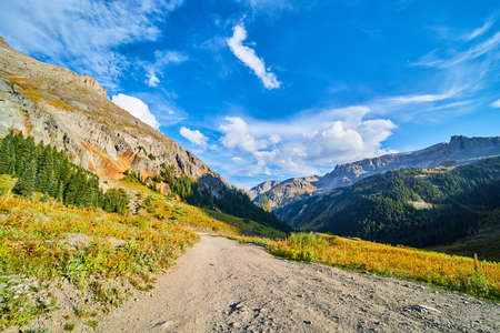 Dirt road high up in the Rocky Mountains with view of valley and mountain rangesの写真素材