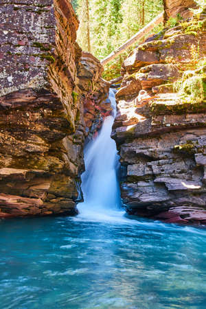 Steep cliffs covered in lichen with waterfall and blue waterの写真素材