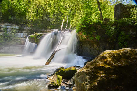 Waterfall cutting through rocks into river with bouldersの写真素材