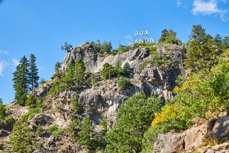 Cliff wall with pine trees and large Box Canon sign at topの写真素材