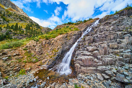 Waterfall over slopped spiky rocks in the colorful fall mountains