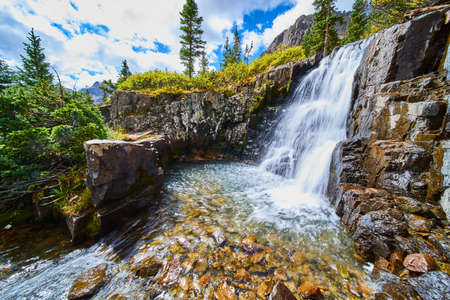 Majestic waterfall into bucket of water surrounded by rocks covered in colorful lichenの写真素材