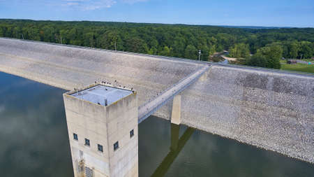 Aerial of a concrete dam with gravel slopes and crows on the rood and on the bride and a forest in...