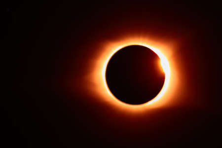 Solar eclipse with solar flare that makes for an orange glow around the black moonの写真素材