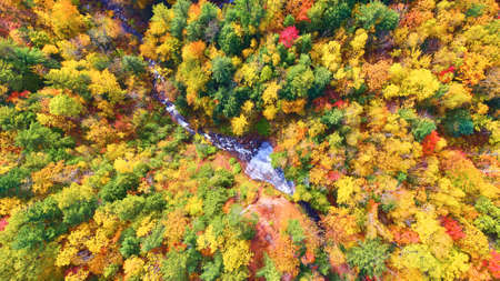 Aerial of waterfall with river and forest below with green, orange, yellow and red trees