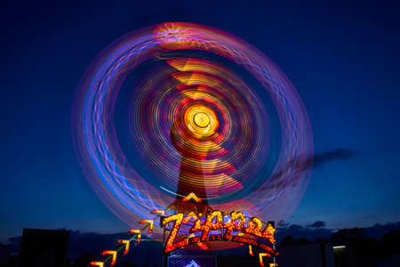 Blue, red, yellow, purple and other lights blurred on the Zipper carnival or fair ride at night