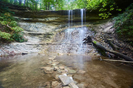 Circular waterfall with a stone path in its basin within a forestの写真素材