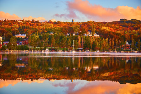 Sail boats and other boats docked on a shoreline bathed in fall colors and with a river reflecting the sceneの写真素材