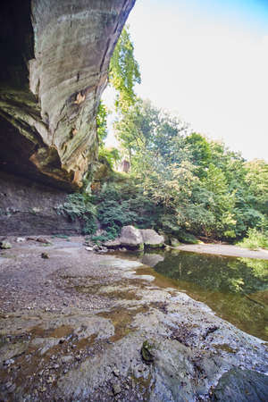 Shallow waterfall basin with overhanging cliff edge in a green forestの写真素材